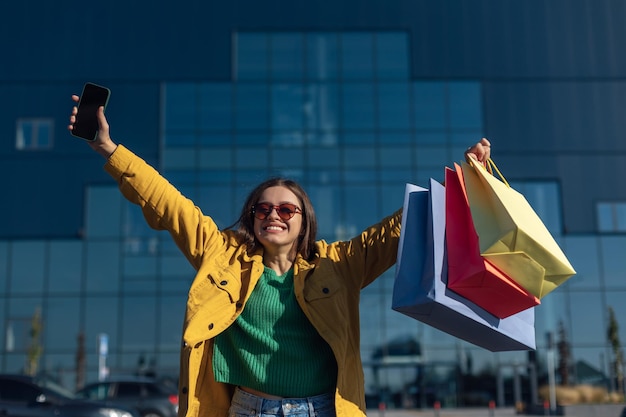 Woman raised hands up with smartphone and shopping bag with a groceries