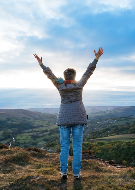 Woman raising hands high and standing on top of mountain