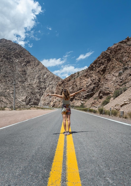 Woman raising her arms on empty road between mountains