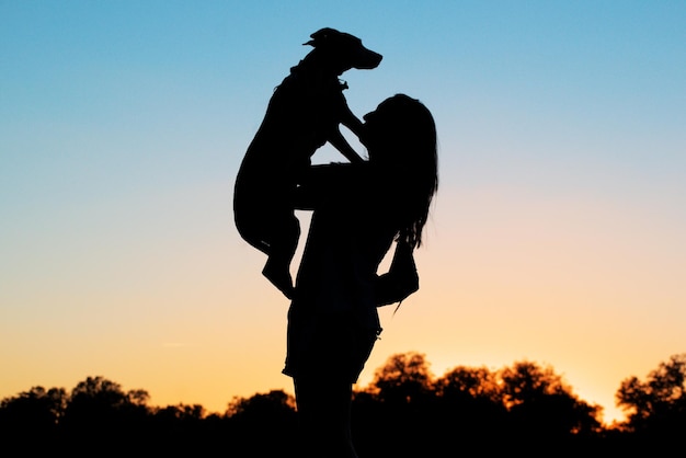 Woman raising her dog as a symbol of love and greatness backlit silhouette in profile