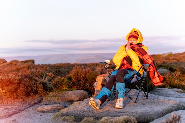 Woman reaching the destination and sitting on beach chairs on top of hill or mountain at sunrise