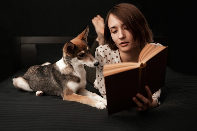 Woman reading book to dog lying on bed