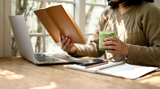 A woman reading a book while enjoying with her iced matcha green tea at a coffee shop