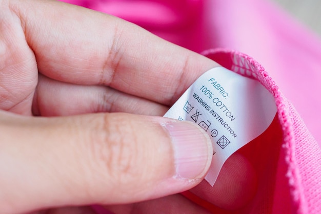 Woman reading on laundry care washing instructions clothes label on pink cotton shirt