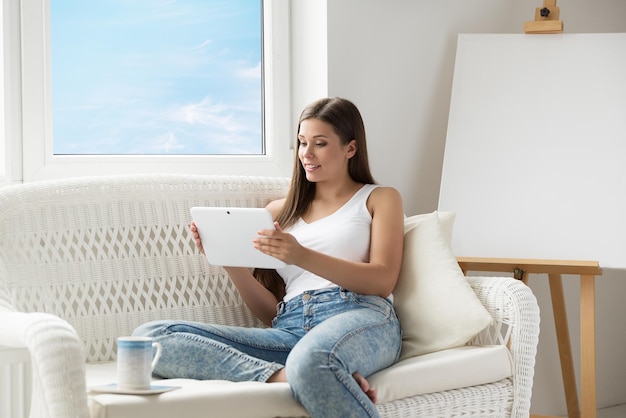 Woman reading Tablet on Sofa at Easel Canvas Girl using Touch Pad Screen resting next to Window