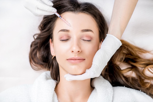 Woman receiving a botox injection in the eye zone lying in bathrobe on the medical couch