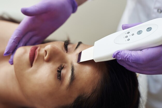 Woman receiving cleansing therapy with a professional ultrasonic equipment in cosmetology office