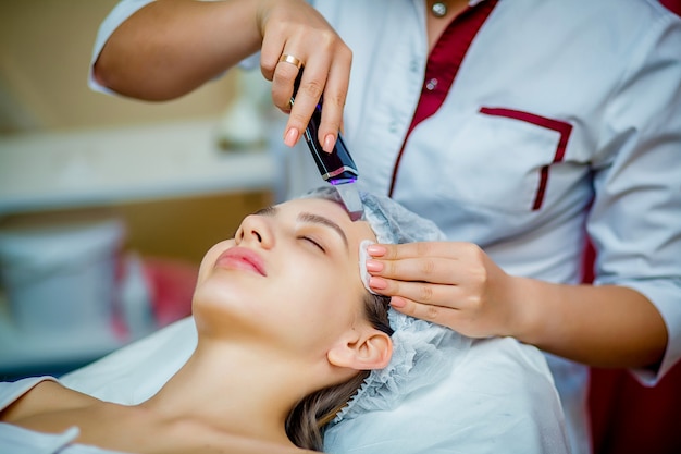 Woman receiving ultrasonic facial exfoliation at cosmetology salon. 