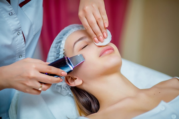 Woman receiving ultrasonic facial exfoliation at cosmetology salon.