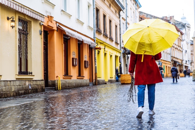 Woman in red coat with yellow umbrella walk by street in rainy weather copy space