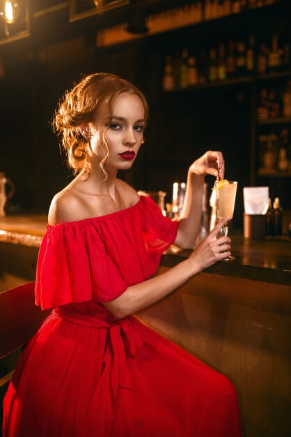 Woman in red dress drinks cocktail at bar counter