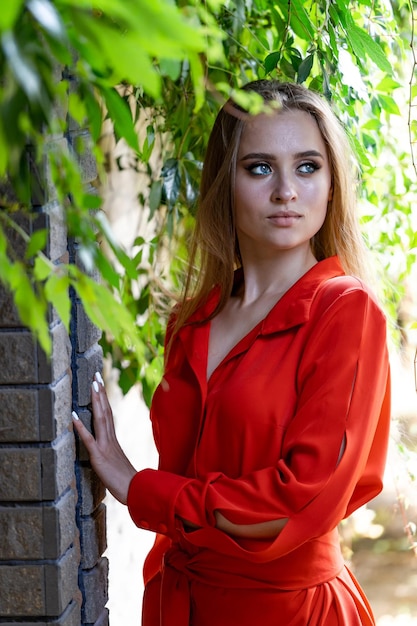 Woman in Red Dress Leaning Against Brick Wall A woman wearing a vibrant red dress poses against a weathered brick wall