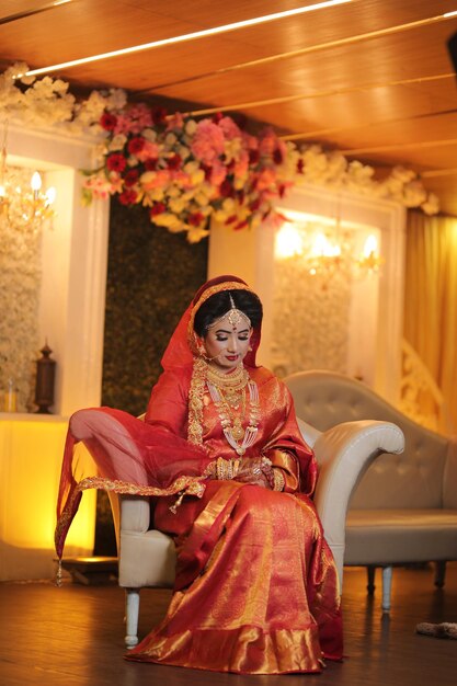 a woman in a red dress sits on a chair with a floral arrangement behind her