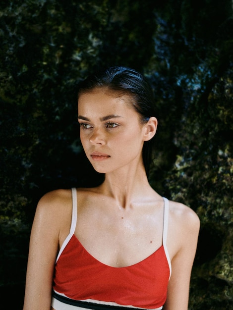 A woman in a red dress stands in front of a mossy wall.