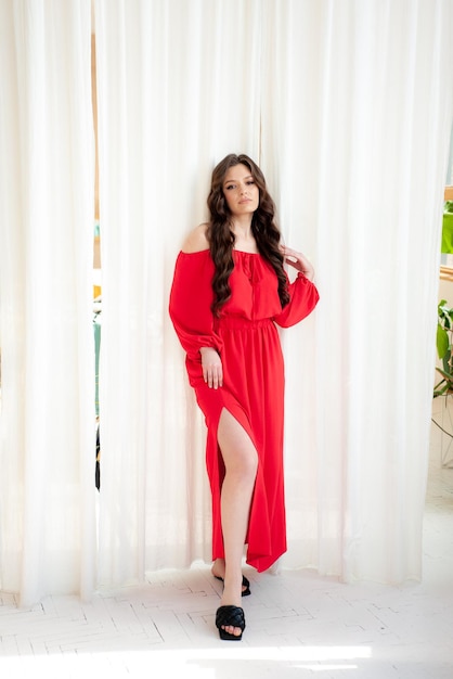 A woman in a red dress stands in front of a white curtain.