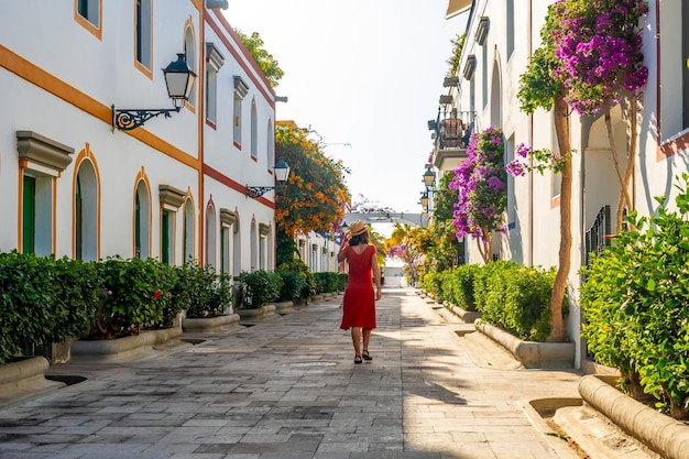 A woman in a red dress walks down a narrow street lined with trees and buildings