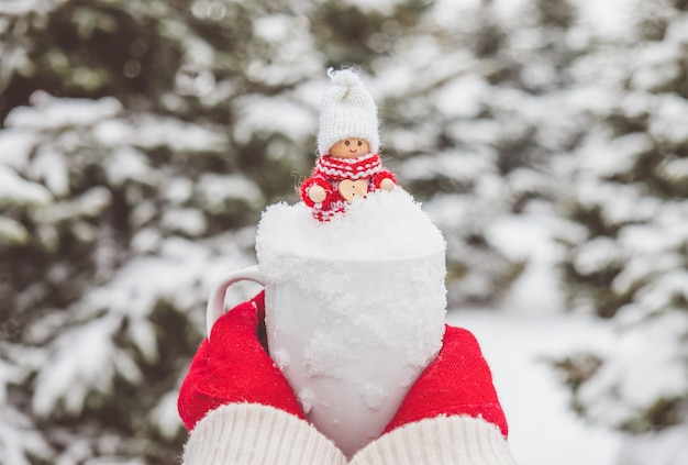 Woman in red gloves is holding the mug with snow and cute christmas toy inside.