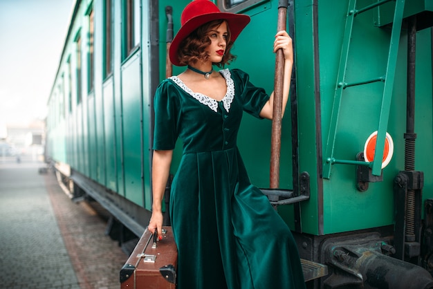 Woman in red hat against old railway wagon. Retro train. Railroad journey