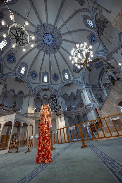 Photo woman in red orange dress stands alone taking photo in small mosque in blue tints istanbul turkiye