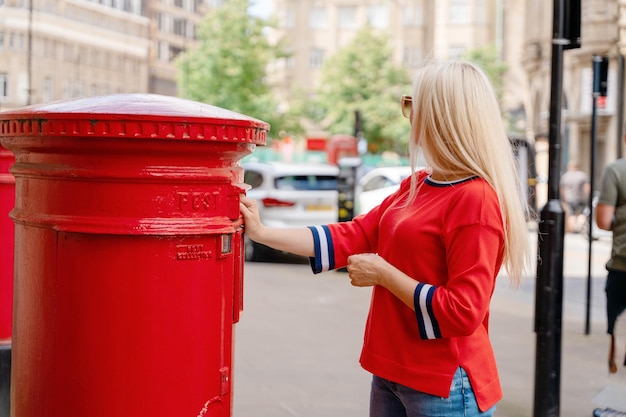 Woman in red short posting letters in red post box in England