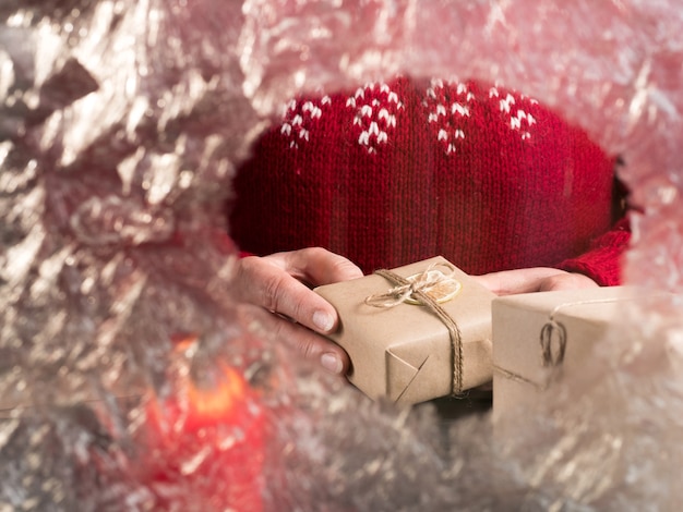 A woman in a red sweater holds gifts behind frozen glass. Christmas holidays.