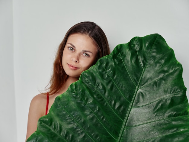 Woman in a red tshirt holds a green leaf in her hand clean skin and