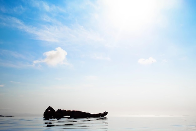 Woman relaxing in infinity swimming pool looking at view