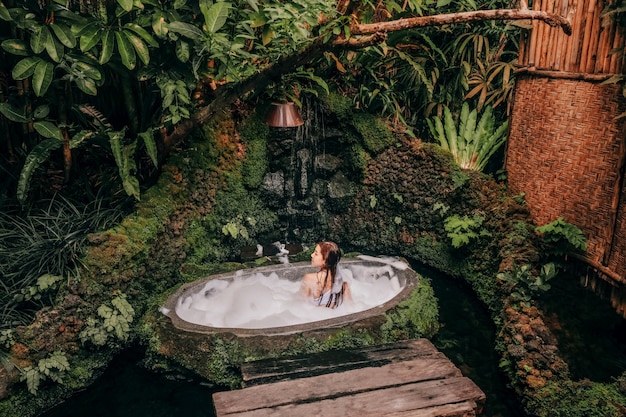 Woman relaxing in outdoor bath with tropical jungle luxury spa hotel