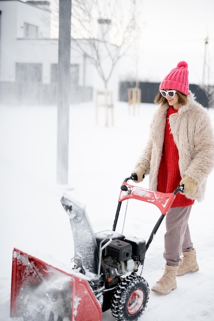 Woman removes snow from pathway with a snow thrower machine