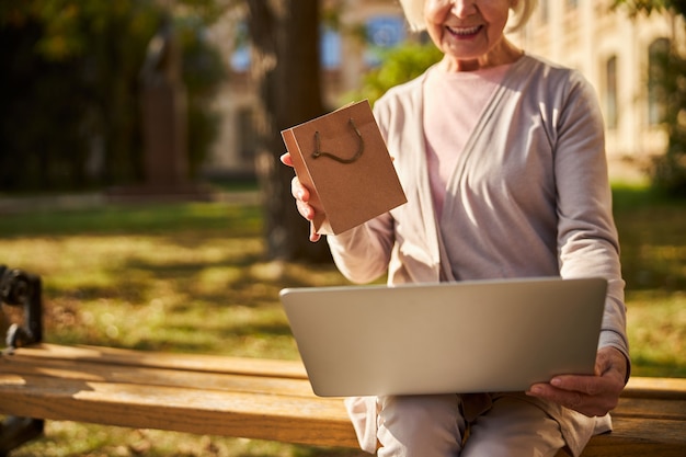 a woman in retirement sitting on a bench in a yard keeping a laptop and a bag