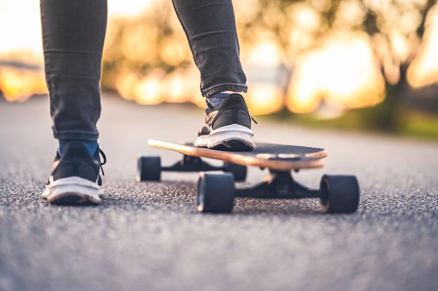 Woman rides at straight road on longboard at sunset time Skater in casual wear training on board during evening sunset with orange light Girl hold longboard in hands