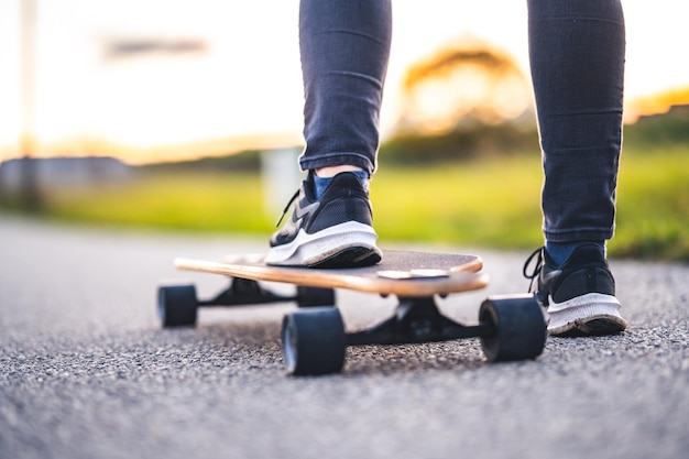 Woman rides at straight road on longboard at sunset time Skater in casual wear training on board during evening sunset with orange light Girl hold longboard in hands