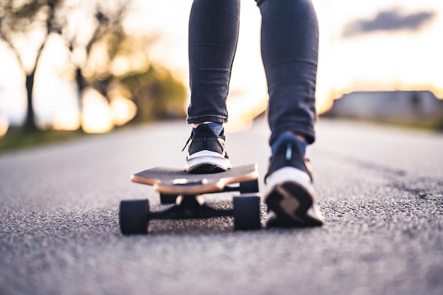 Woman rides at straight road on longboard at sunset time Skater in casual wear training on board during evening sunset with orange light Girl hold longboard in hands