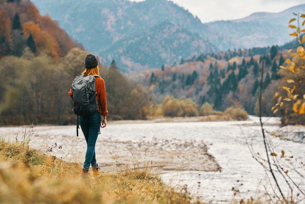 Woman on the river bank in the mountains in the autumn forest in nature back view