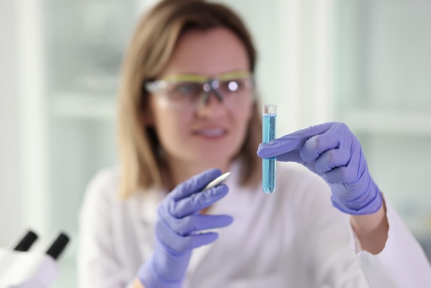 Woman in rubber gloves holds glassware with blue chemical liquid for scientific research