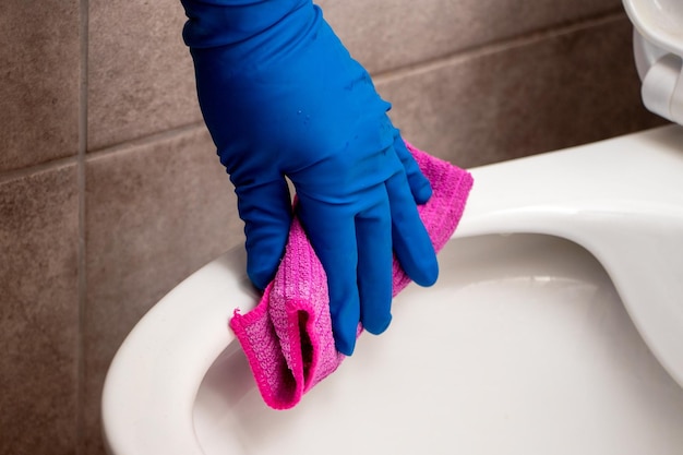 A woman in rubber gloves wipes the lavatory pan with a rag