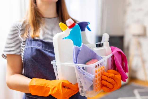 Woman in rubber gloves with basket of cleaning supplies ready to clean up