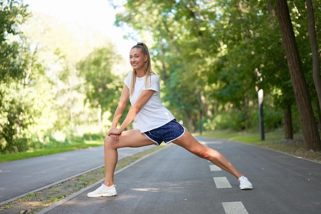 Woman runner stretching legs before exercising summer park morning