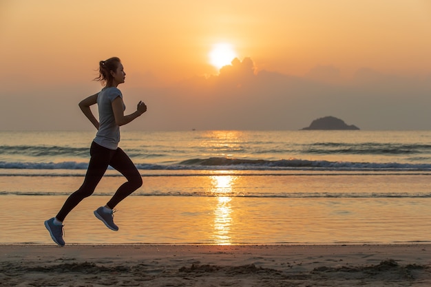 Woman running on beach at sunrise with water and wave in background.