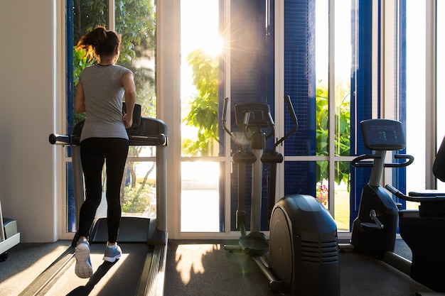 Woman running in fitness gym on treadmill exercise equipment.