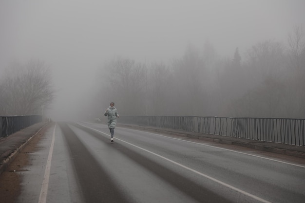 A woman runs along a foggy road on an autumn day misty road