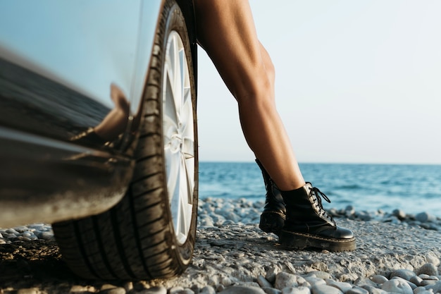 Woman's feet standing by car near sea