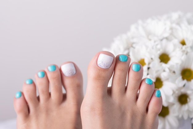 A woman's feet with turquoise and white nail polish and a white flower in the background