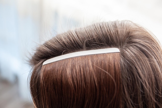 A woman's hair is wearing a white headband with a silver band in the middle.