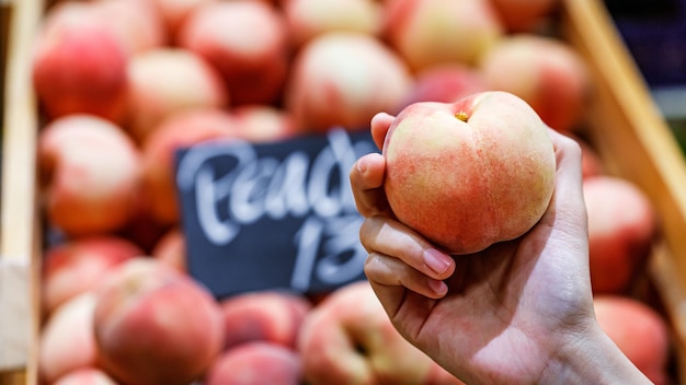 Woman's hand choosing peach fruit in supermarket