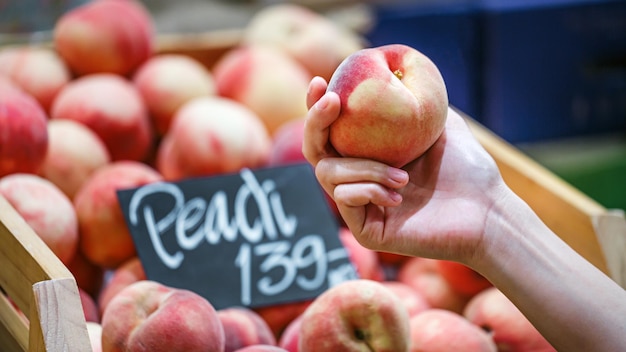 Woman's hand choosing peach fruit in supermarket