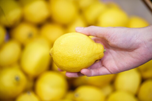 Woman's hand choosing yellow lemon fruit in supermarket