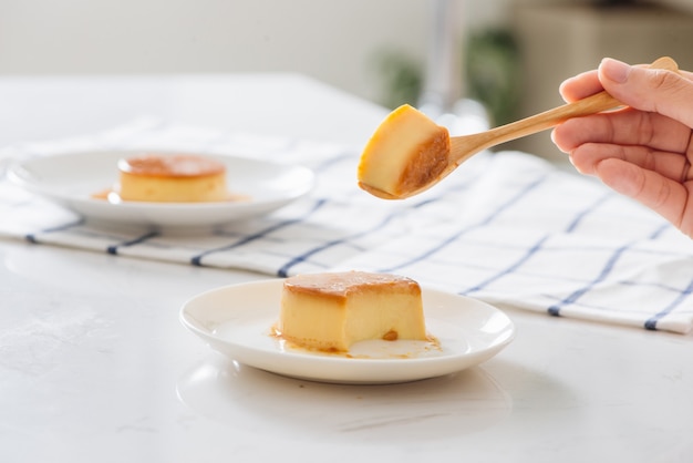 Woman's hand cutting homemade caramel custard pudding on white plate