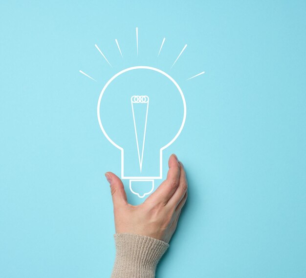 Photo woman's hand and a drawn electric lamp on a blue background the concept of searching for ideas and solutions brainstorming switching to alternative forms of energy