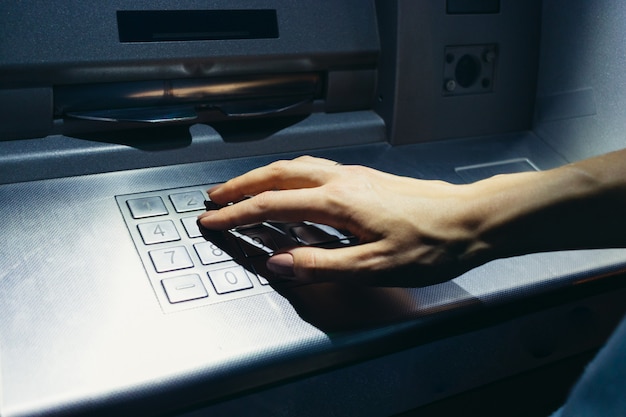 Woman's hand enters the secret code at the ATM on the street at night